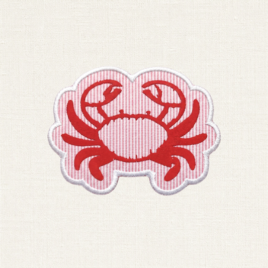 A close-up of a crab shaped embroidered patch. In the center is a red crab, set against a background of alternating horizontal stripes similar to seersucker. The entire patch is enclosed by a clean, raised white merrowed border.

Red crab design on a white background