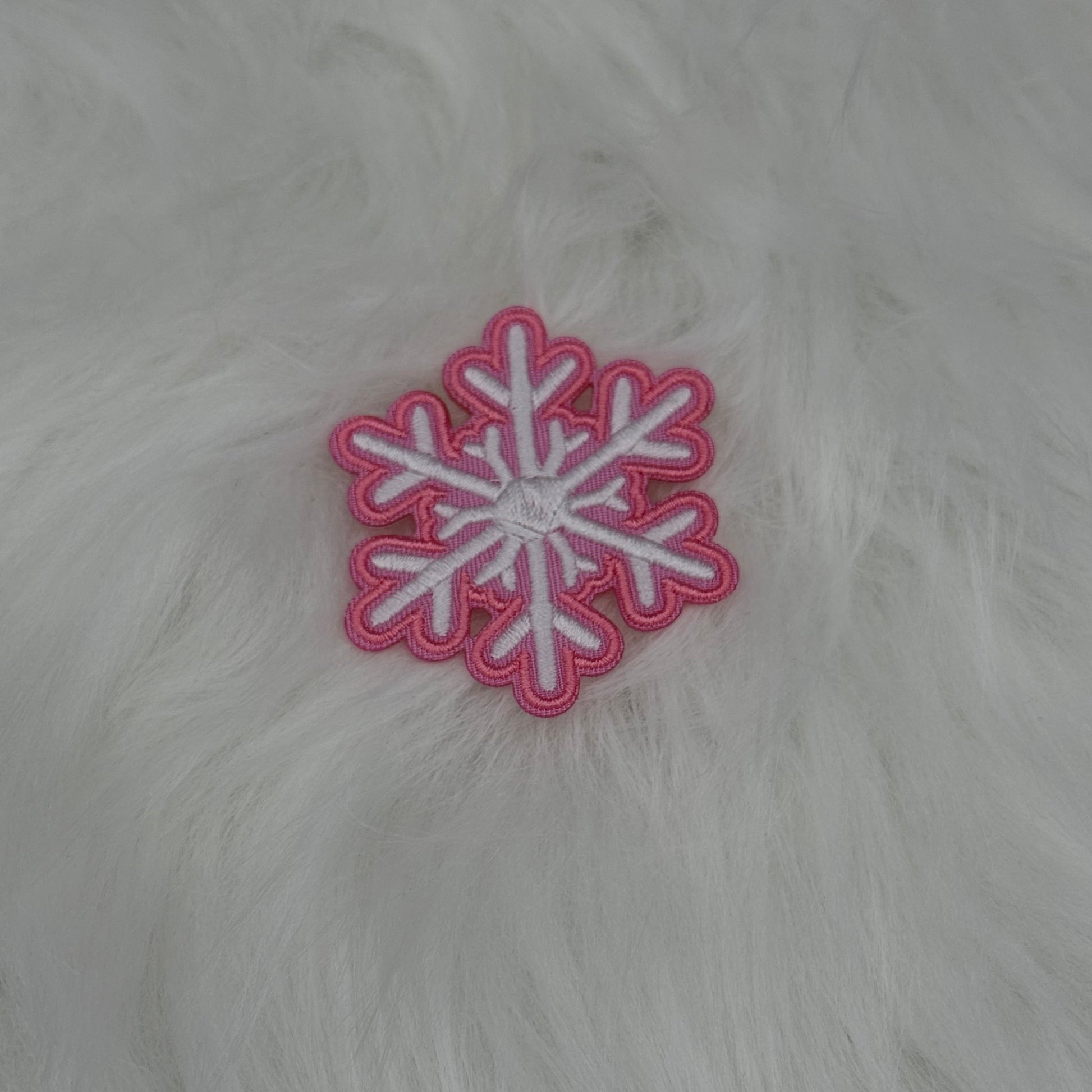 Pink and white snowflake patch on a white fur background.

The patch is embroidered. The patch colors are pink and white. This is displayed on a fluffy white fur blanket. 

Great for winter and après ski clothing, bags, accessories and gifts!