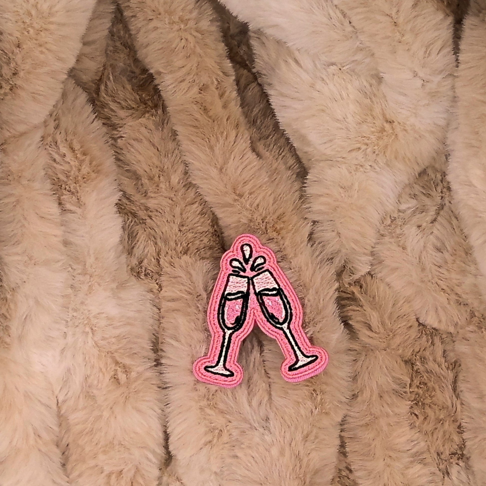 Pink and white champagne glass embroidered patch on a beige fur background

The patch is embroidered. The patch colors are pink and white with pale pale pink accents. There are 2 champagne glasses doing a "cheers". This is displayed on a fluffy brown fur blanket. 

Great for winter and après ski clothing, bags, accessories and gifts!
